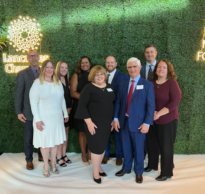 A group of Brown Plus team members in formal dress posing in front of a decorative green wall